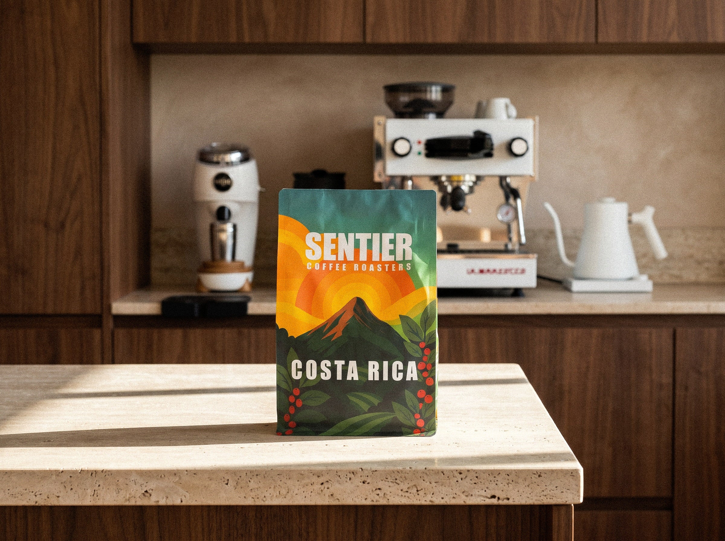 Coffee bag labeled 'Sentier Coffee Roasters Costa Rica' on a kitchen counter with coffee-making equipment in the background.