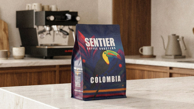 Sentier Coffee Roasters Colombia coffee bag on a kitchen counter with a coffee machine in the background.